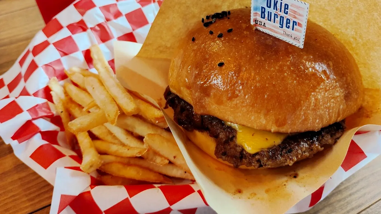 店名フラッグを立てたハンバーガーと赤白チェック紙の上のポテト、コーラ