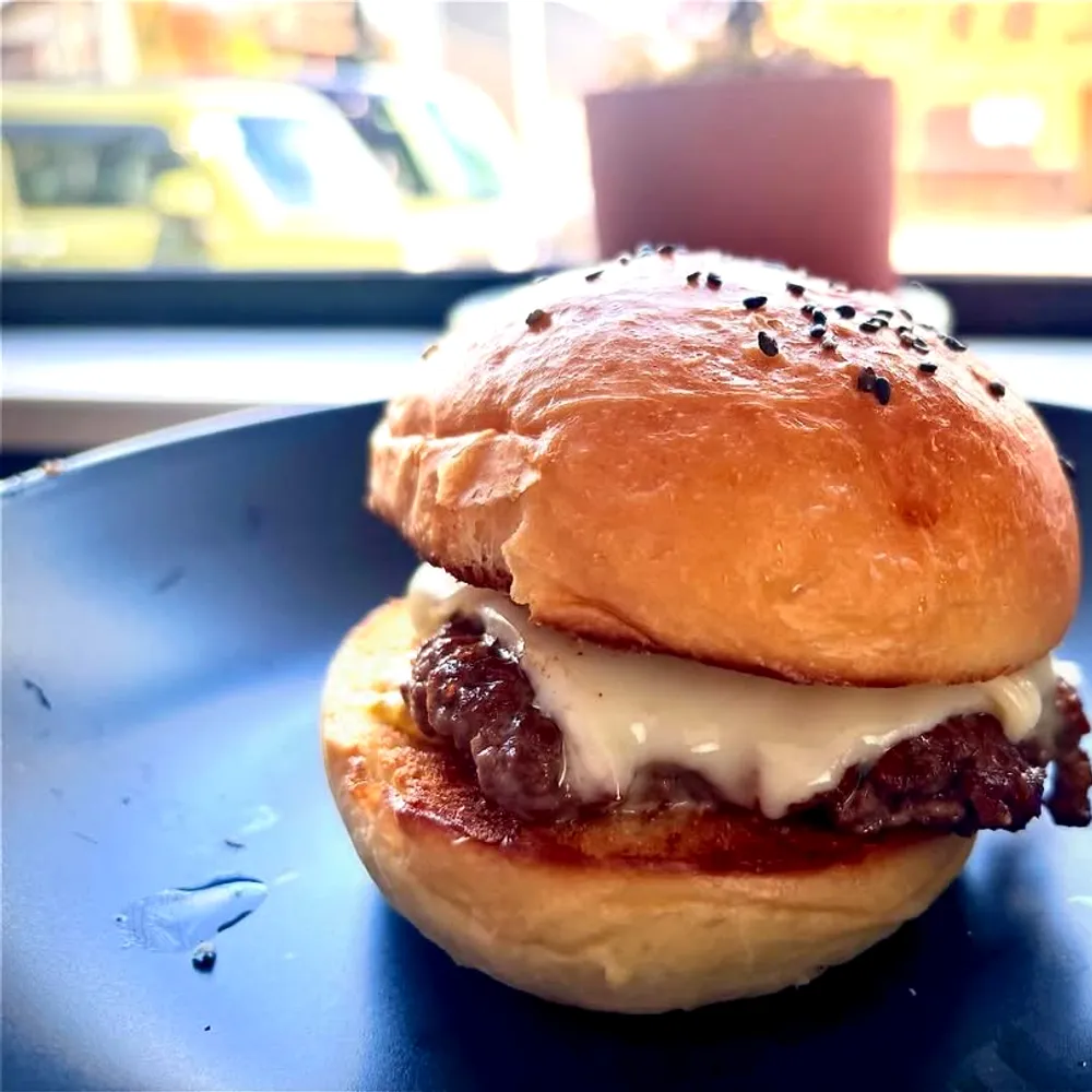 ネイビーの皿にのったチーズバーガー。窓越しの光を受けた看板カット